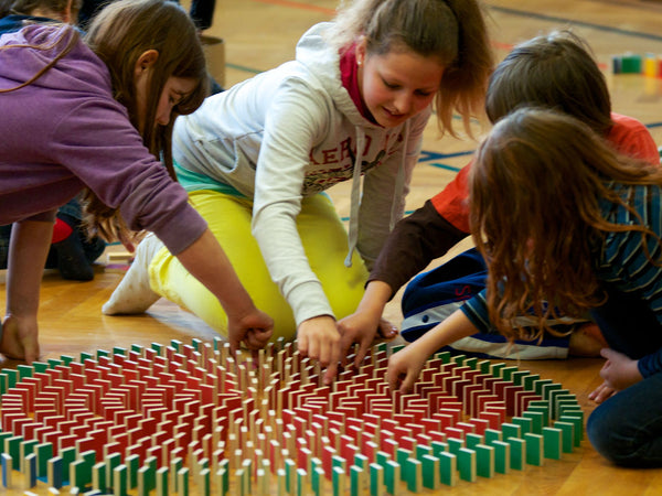 Vier Mädchen zwischen 9 und 13 Jahren bauen gemeinsam sehr geschickt an einer großen Spirale aus PESTAS Dominosteinen