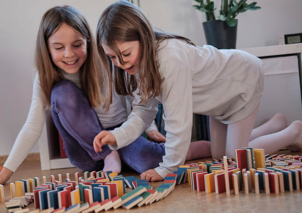 Zwei  Mädchen beobachten begeistert, wie ihre PESTAS-Dominobahn umfällt.